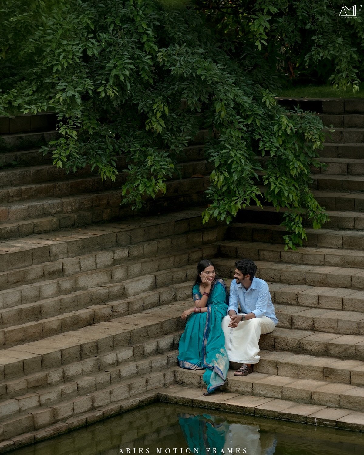 A couple sitting together on stone steps beneath lush trees