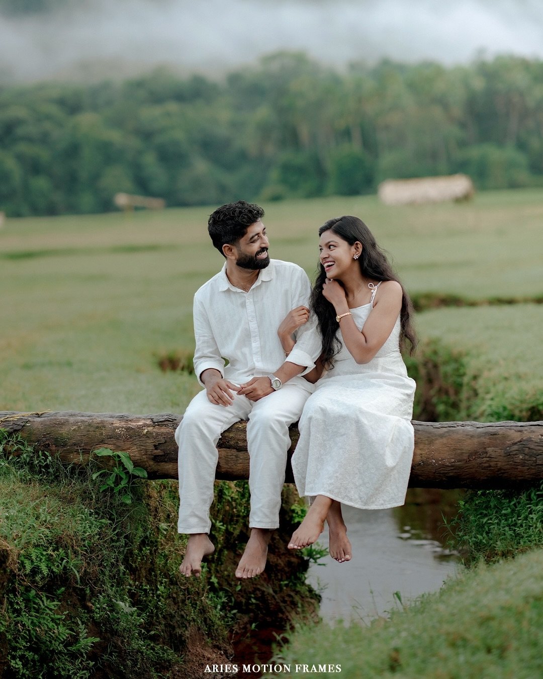 A couple sitting together on a log in a green countryside landscape